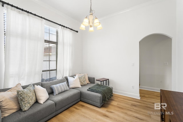 living room featuring baseboards, arched walkways, ornamental molding, light wood-style floors, and a notable chandelier