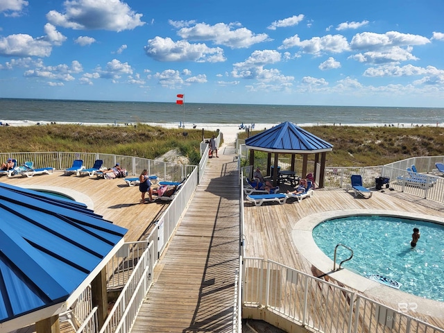 view of swimming pool with a gazebo, a deck with water view, and a beach view