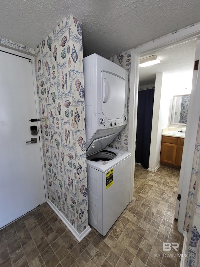 laundry area with a textured ceiling, stacked washer / drying machine, and sink