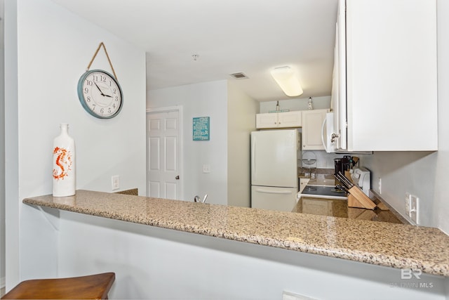 kitchen with white appliances, kitchen peninsula, light stone counters, and white cabinets