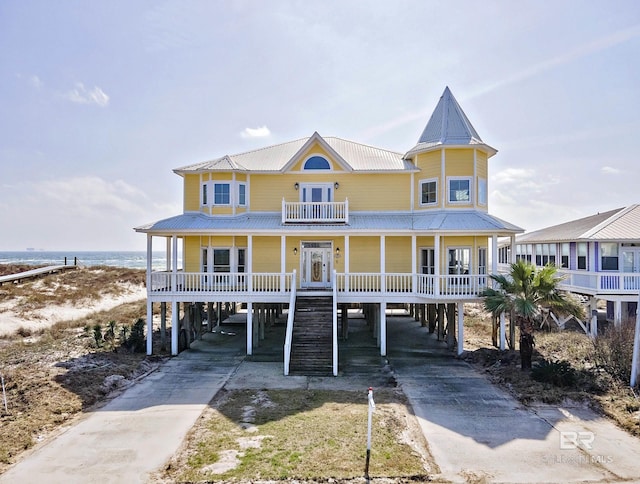 raised beach house with a carport, covered porch, driveway, and metal roof