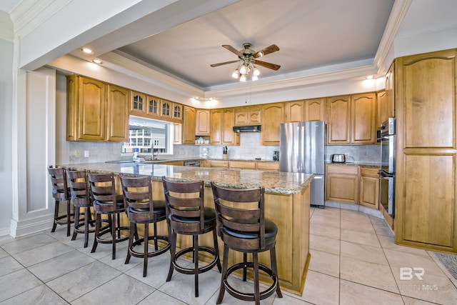 kitchen featuring a peninsula, a kitchen bar, appliances with stainless steel finishes, and a tray ceiling