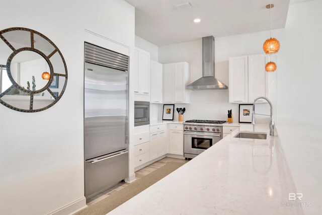 kitchen with white cabinetry, built in appliances, pendant lighting, sink, and wall chimney range hood