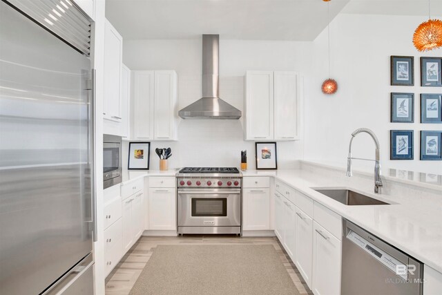 kitchen with hanging light fixtures, white cabinetry, wall chimney exhaust hood, premium appliances, and sink