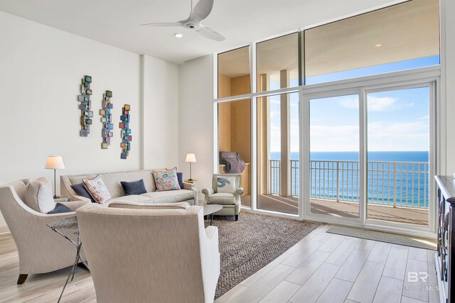 living room with light wood-type flooring, a water view, ceiling fan, and expansive windows