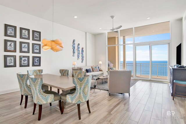 dining space with ceiling fan, a wall of windows, and light wood-type flooring