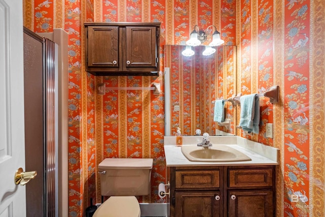 bathroom with toilet, wallpapered walls, and vanity