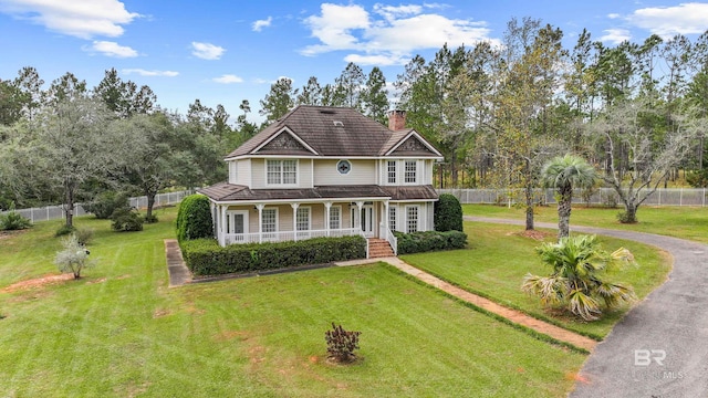 view of front of home with a porch, a chimney, a front yard, fence, and aphalt driveway