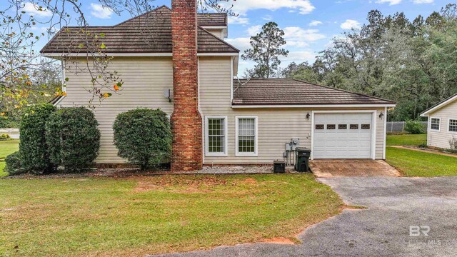 exterior space with an attached garage, aphalt driveway, a yard, and a chimney