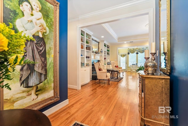 hallway with built in shelves, a tray ceiling, light hardwood / wood-style flooring, and ornamental molding