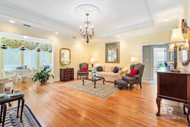 living room featuring light hardwood / wood-style floors, an inviting chandelier, ornamental molding, and a tray ceiling