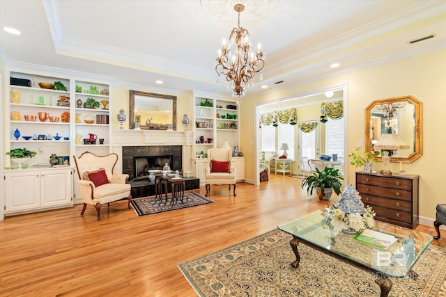 living room featuring light wood-type flooring, ornamental molding, a raised ceiling, a notable chandelier, and a fireplace