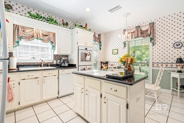 kitchen with white cabinets, a healthy amount of sunlight, a kitchen island, and white appliances