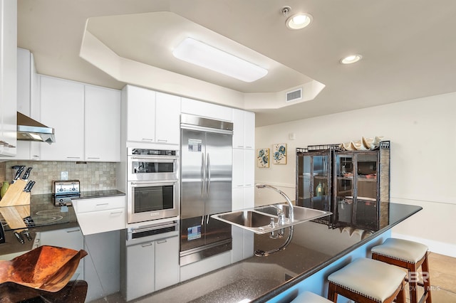 28107 Perdido Beach Blvd Unit D1005, Orange Beach, AL 36561 - kitchen with appliances with stainless steel finishes, a breakfast bar area, tasteful backsplash, white cabinetry, and ventilation hood