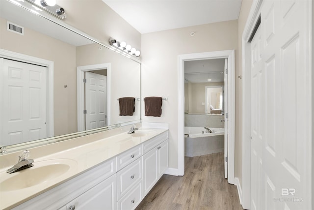 bathroom featuring double vanity, wood finished floors, a sink, and a bath