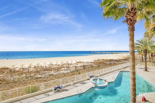 view of swimming pool featuring a beach view, fence, a pool with connected hot tub, a water view, and a patio area