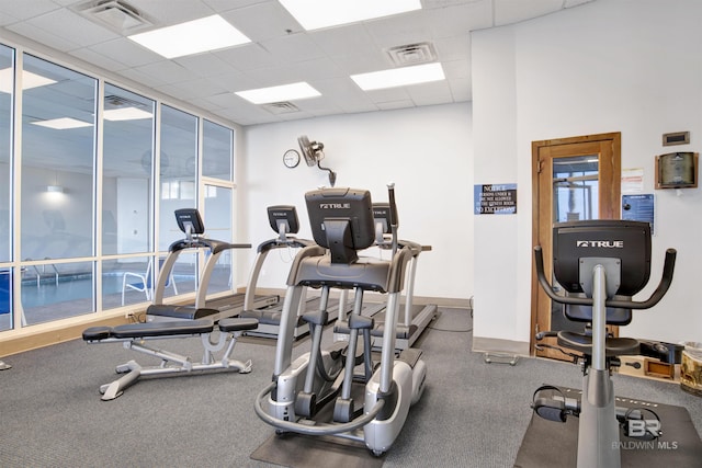 exercise room featuring a paneled ceiling, visible vents, and a wall of windows