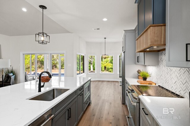 kitchen with light stone counters, sink, decorative light fixtures, and appliances with stainless steel finishes