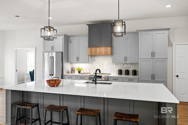 kitchen with sink, high quality fridge, gray cabinetry, and an island with sink