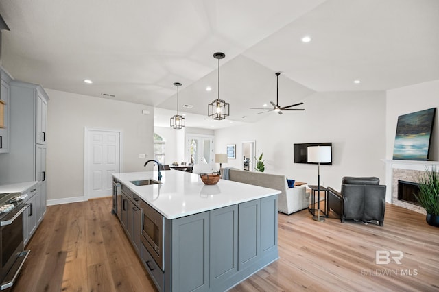 kitchen with appliances with stainless steel finishes, sink, decorative light fixtures, a stone fireplace, and an island with sink