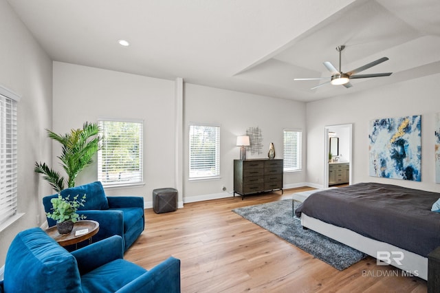 bedroom featuring a raised ceiling, connected bathroom, light hardwood / wood-style flooring, and ceiling fan