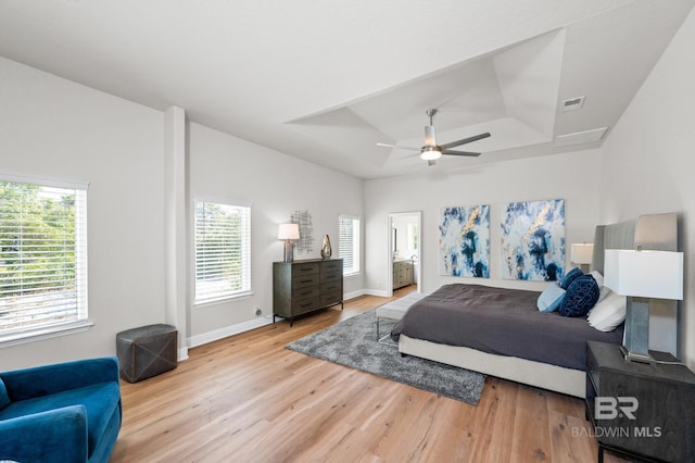 bedroom featuring hardwood / wood-style floors, ceiling fan, multiple windows, and a tray ceiling