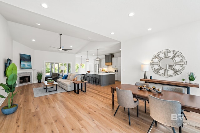 living room with ceiling fan, light hardwood / wood-style flooring, a fireplace, and vaulted ceiling