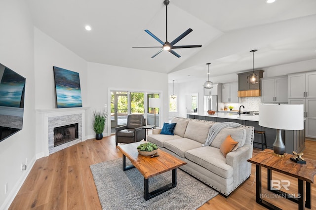 living room featuring light wood-type flooring, vaulted ceiling, ceiling fan, sink, and a stone fireplace