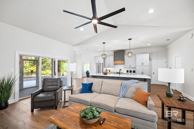 living room with light wood-type flooring, vaulted ceiling, ceiling fan, and sink