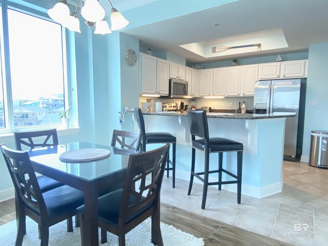 1010 W Beach Blvd Unit 209, Gulf Shores, AL 36542 - dining room featuring a chandelier, a raised ceiling, baseboards, and light wood-style flooring