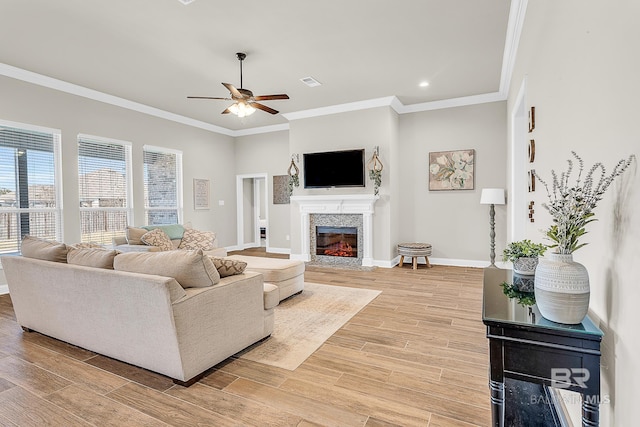 living area featuring a fireplace, ornamental molding, a ceiling fan, light wood-type flooring, and baseboards