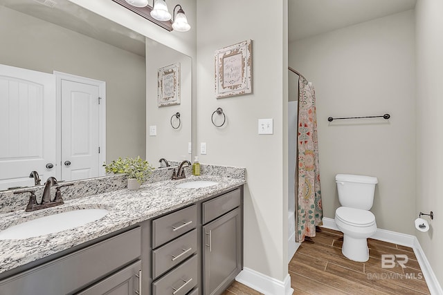 bathroom featuring double vanity, wood finished floors, a sink, and baseboards