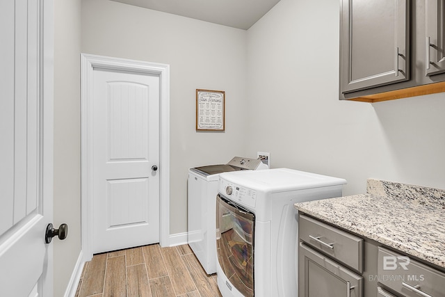 laundry room with cabinet space, washing machine and dryer, baseboards, and light wood-style flooring