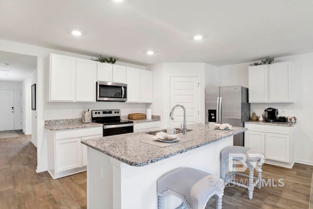 kitchen with white cabinetry, an island with sink, light hardwood / wood-style floors, and stainless steel appliances