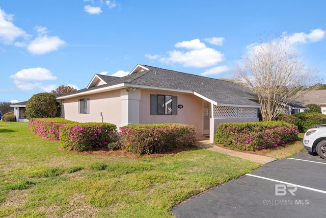 view of front of home with stucco siding, roof with shingles, uncovered parking, and a front yard