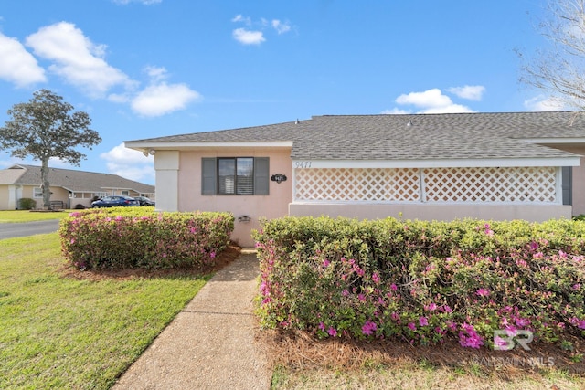 view of front of property with stucco siding, a front yard, and roof with shingles