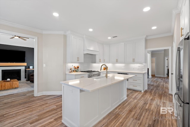 kitchen featuring white cabinetry, a center island with sink, custom range hood, and appliances with stainless steel finishes