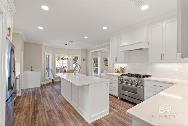 kitchen featuring custom range hood, stainless steel appliances, pendant lighting, a center island with sink, and white cabinets