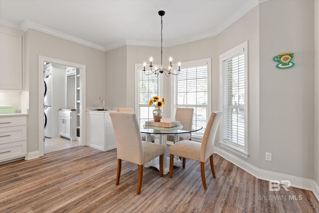 dining space with a chandelier, light hardwood / wood-style floors, crown molding, and stacked washer and clothes dryer