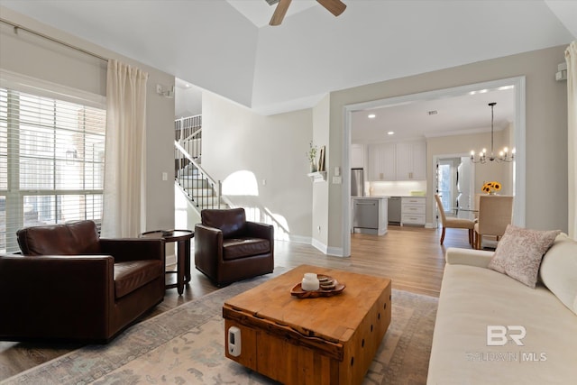 living room with ceiling fan with notable chandelier, lofted ceiling, and light hardwood / wood-style flooring