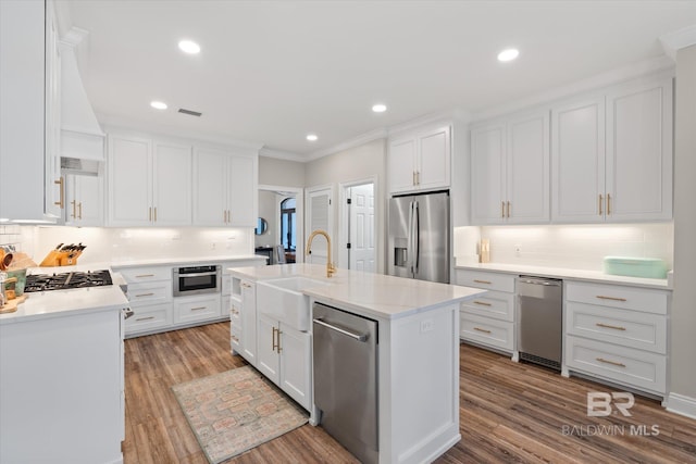 kitchen with appliances with stainless steel finishes, sink, hardwood / wood-style floors, white cabinetry, and an island with sink