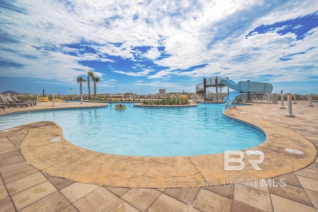 community pool with fence, a water slide, and a patio