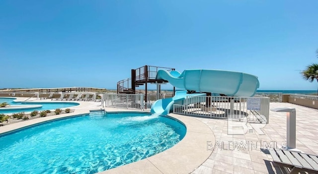 community pool featuring fence, a water slide, and a patio area