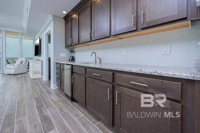 kitchen featuring a sink, dark brown cabinetry, backsplash, and light wood-type flooring