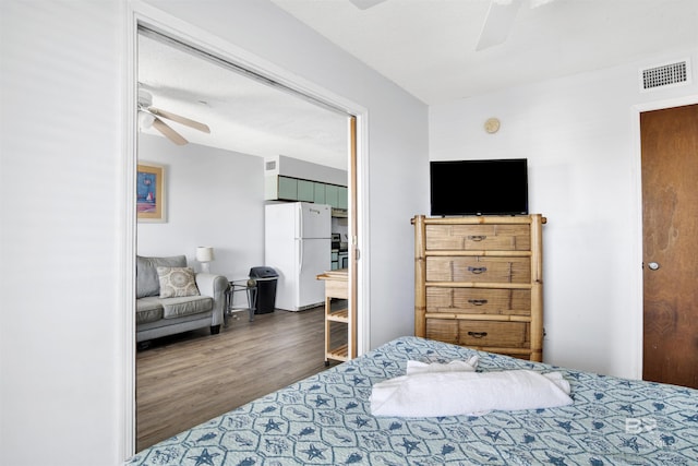 bedroom featuring a ceiling fan, freestanding refrigerator, visible vents, and wood finished floors