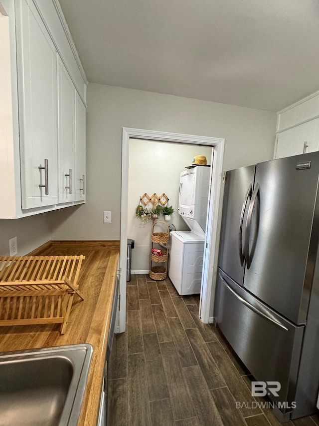 kitchen featuring stainless steel refrigerator, white cabinetry, sink, stacked washing maching and dryer, and wooden counters