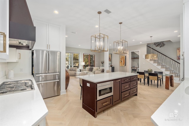 kitchen featuring white cabinetry, a center island, hanging light fixtures, appliances with stainless steel finishes, and custom range hood