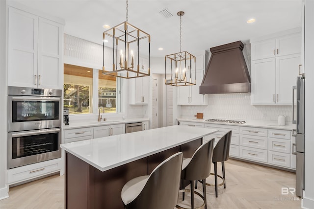 kitchen with sink, a breakfast bar area, white cabinetry, stainless steel appliances, and custom exhaust hood