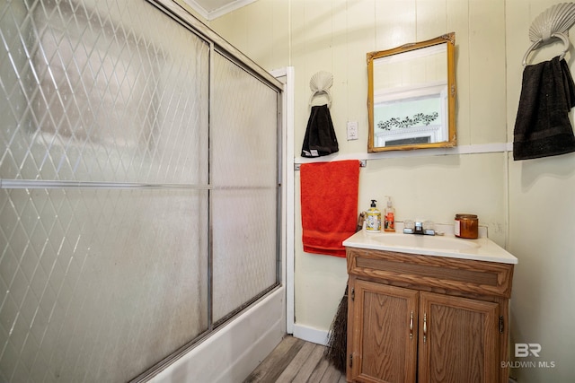 bathroom featuring hardwood / wood-style floors, vanity, crown molding, and bath / shower combo with glass door