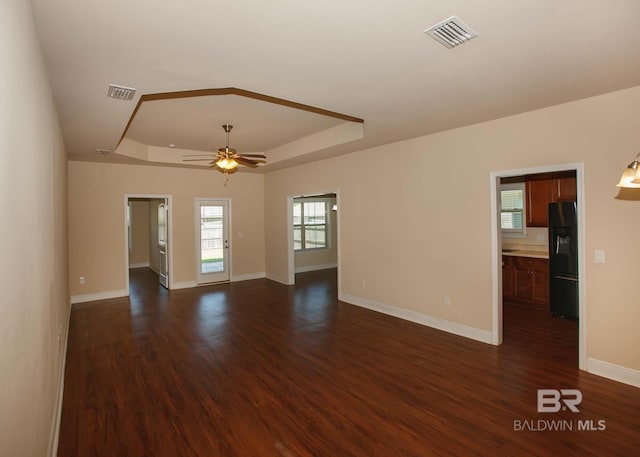 unfurnished living room featuring ceiling fan, dark hardwood / wood-style flooring, and a tray ceiling